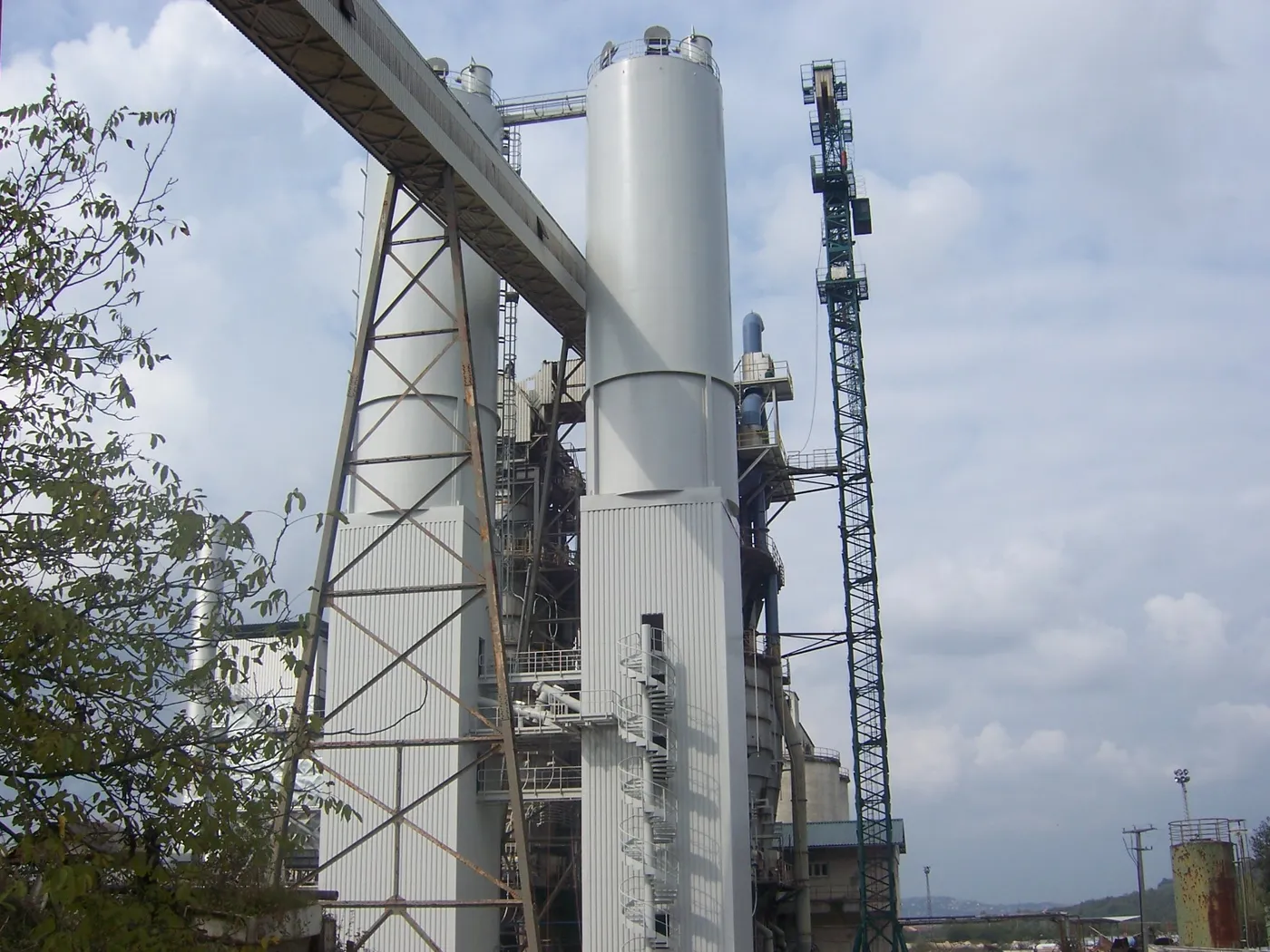 Hohes Stahlsilo neben Förderbrücke und Turmdrehkran in einem Kalkwerk