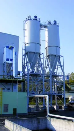 Zwei Silos mit Konus auf Stützgerüst neben einem Anlagengebäude